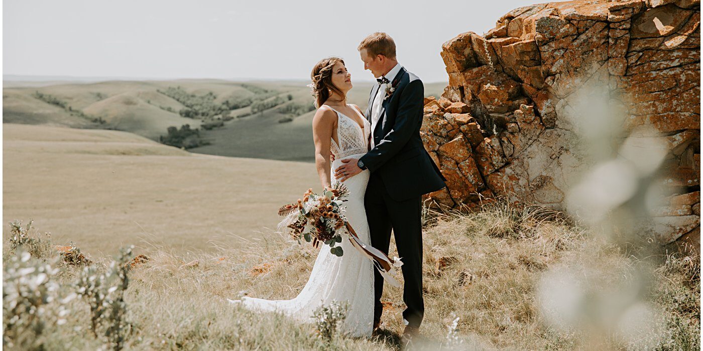 wedding couple portrait holding floral bouquet in a field